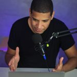 African American man hosts a podcast in a home studio using a microphone and laptop.