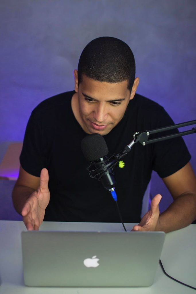 African American man hosts a podcast in a home studio using a microphone and laptop.